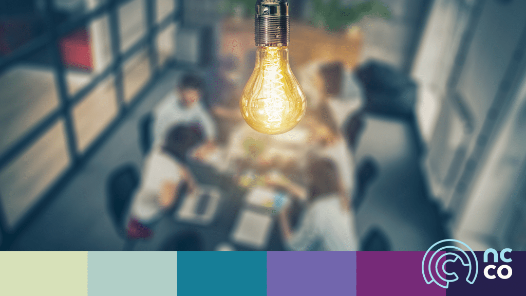Blurred out photo of office workers sitting around a meeting table with an image of a bright lightbulb superimposed on it